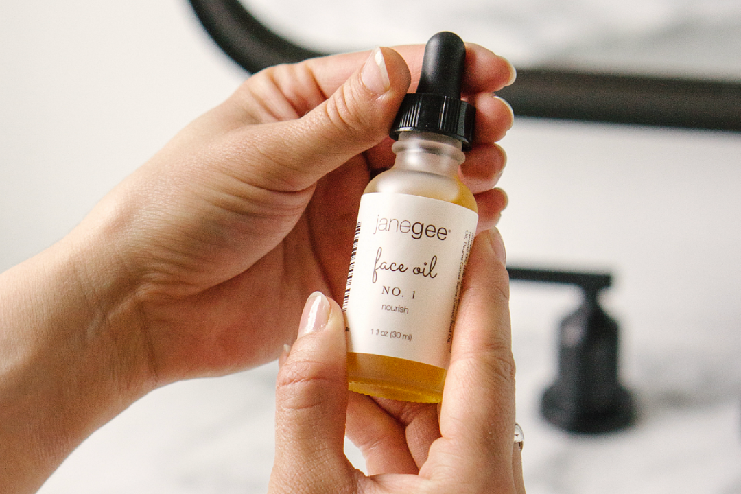 close-up of hands holding a janegee face oil bottle with dropper, highlighting the golden oil and clean, minimal packaging in a soft, natural bathroom setting