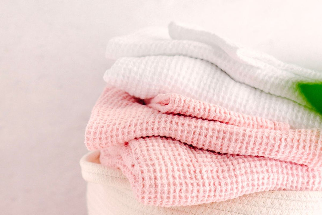 Stack of soft waffle-knit towels in white and blush pink folded on a neutral surface.