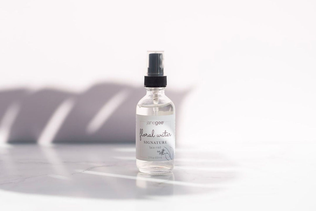 Bottle of janegee signature floral water face mist with spray top on a marble surface, lit by soft natural light.
