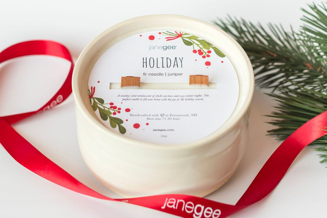 janegee holiday candle with wooden wick in a ceramic vessel, styled with a red ribbon and evergreen sprig on a festive background