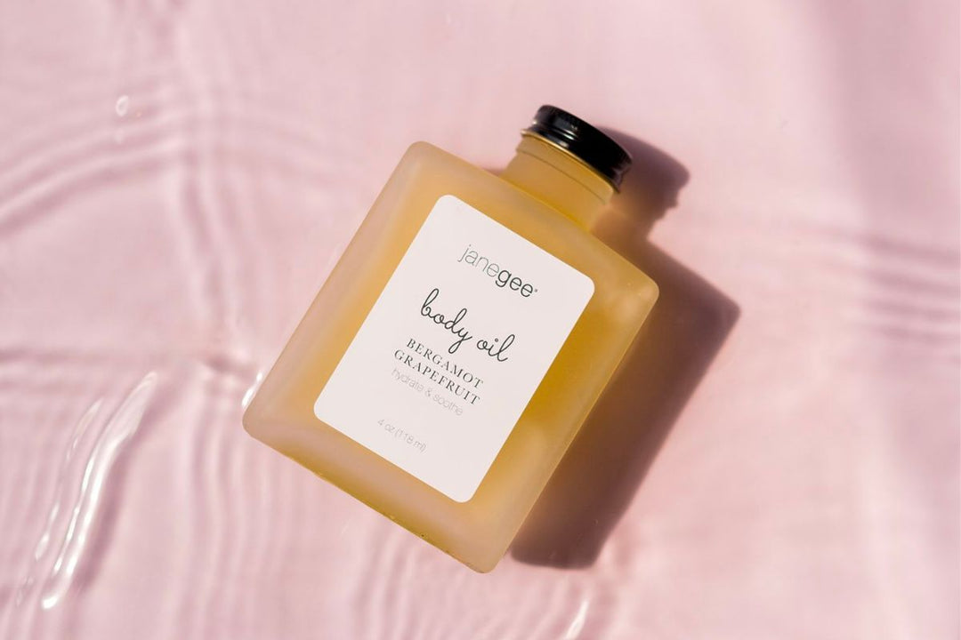 janegee bergamot grapefruit body oil on a blush background with soft water ripples and warm, sunlit glow