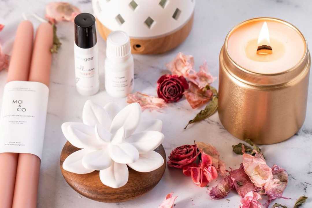 a curated self-care scene featuring a lit gold candle, essential oils, and a ceramic diffuser surrounded by dried roses, creating a warm, calming atmosphere with soft, romantic styling