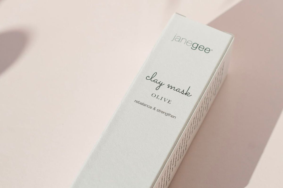 janegee clay mask olive in minimalist packaging, softly lit against a blush-toned background