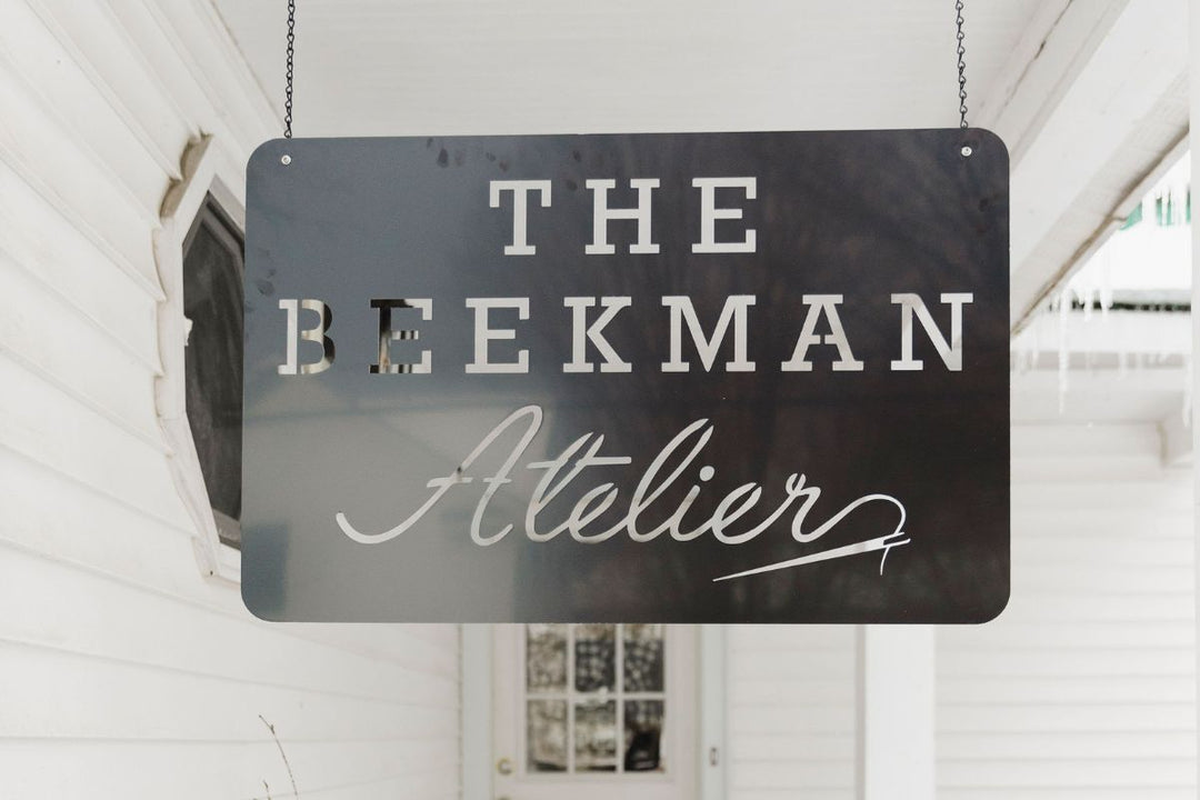 Black hanging sign reading “The Beekman Atelier” displayed outside a white building entrance.