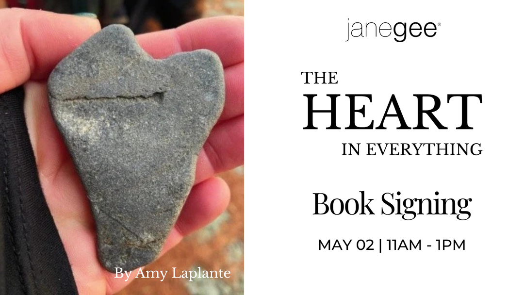 Promotional graphic for “The Heart in Everything” book signing featuring a hand holding a heart-shaped stone alongside event details for May 2 from 11 AM to 1 PM by Amy Laplante