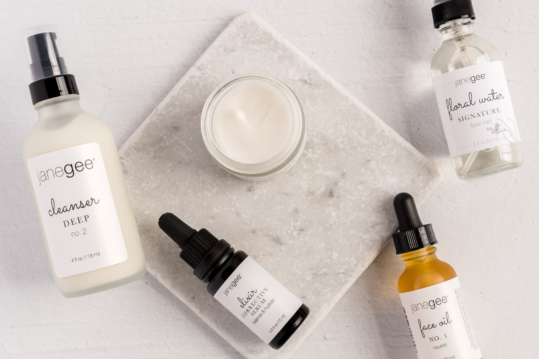 Flat lay of janegee skincare: cleanser, cream, serum, face oil, and floral water.