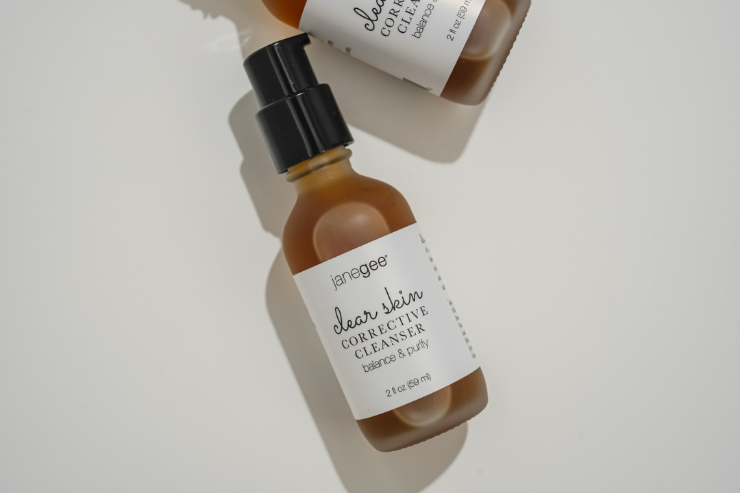 Softly lit flat lay of janegee Clear Skin Corrective Cleanser bottles on a white background, highlighting the amber glass packaging and minimalist label design.