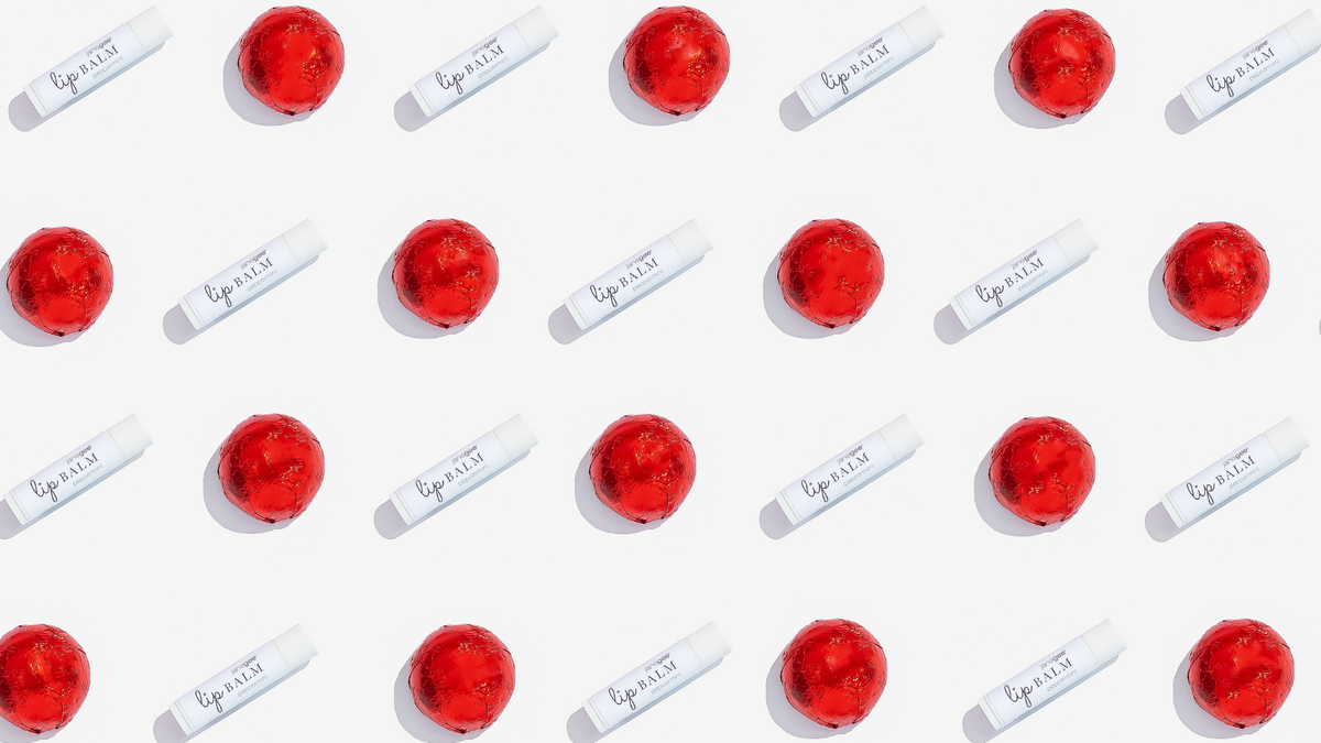 Repeating holiday pattern of janegee Peppermint Lip Balm and red foil-wrapped chocolates on a white background.