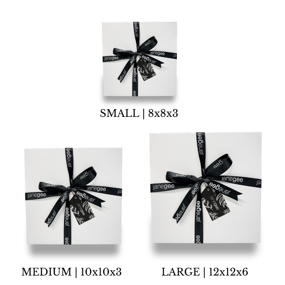 Three white janegee gift boxes in small, medium, and large sizes wrapped with black branded ribbon and decorative gift tags.