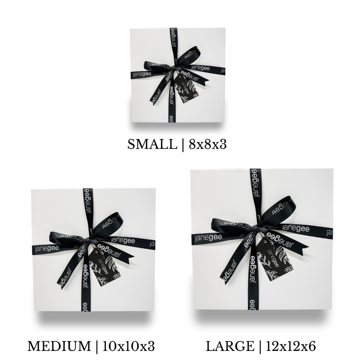 Three white janegee gift boxes in small, medium, and large sizes wrapped with black branded ribbon and decorative gift tags.