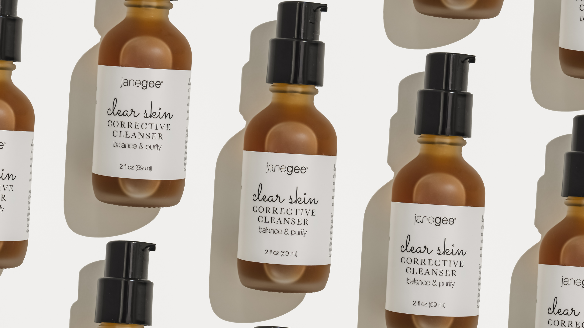 Patterned layout of amber glass janegee Clear Skin Corrective Cleanser bottles with black pumps on a soft neutral background.