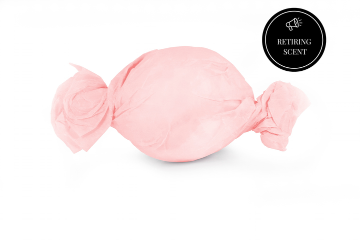A bath bomb wrapped in light pink tissue paper on a white background.
