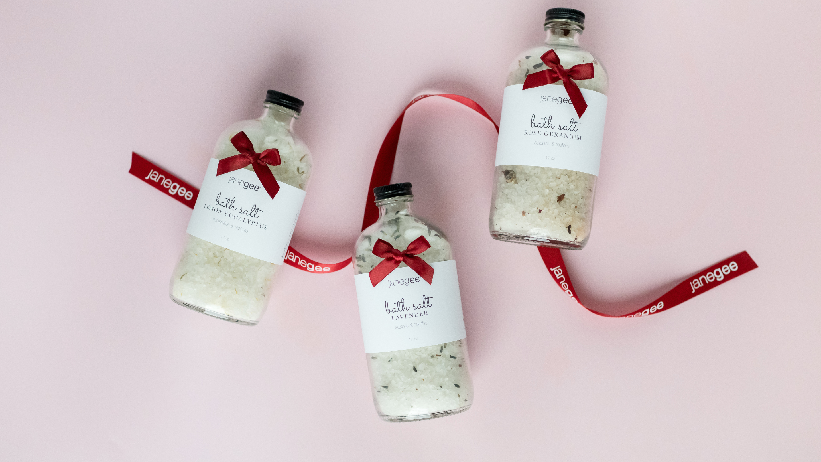 Three bottles of bath salts with red ribbons on a pink background