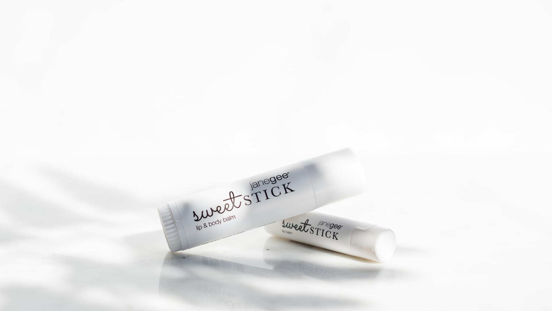 Two white lip balm tubes labeled 'Sweet Stick' by janegee, arranged diagonally on a clean white surface with soft shadows.