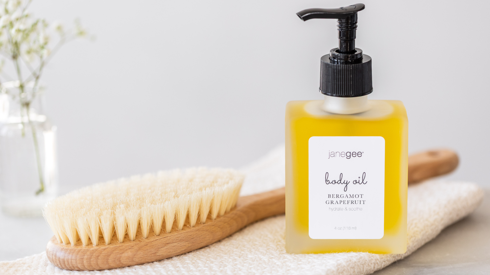Body oil bottle with pump, brush, and towel on a light background