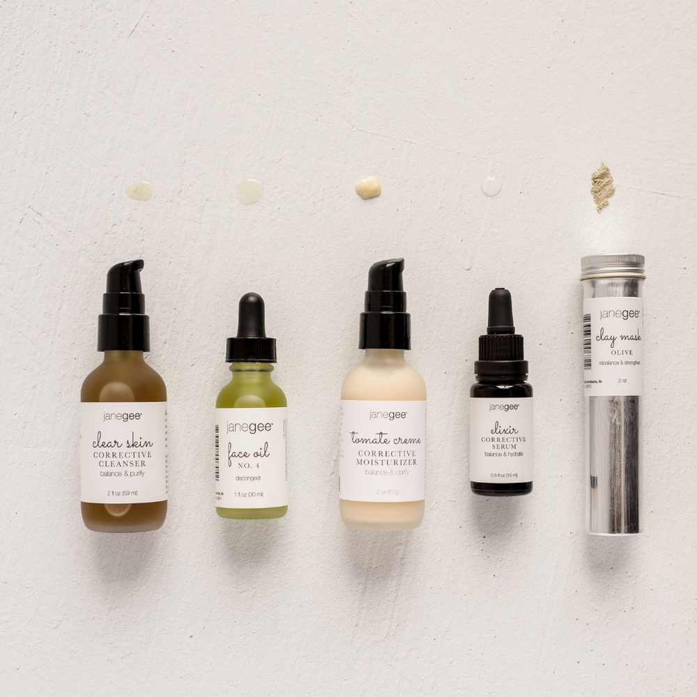janegee skincare lineup with cleanser, face oil, moisturizer, serum, and clay mask with product samples displayed above