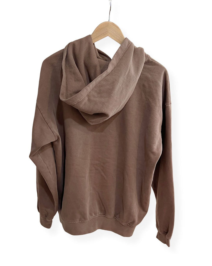 Back view of a brown, oversized fleece janegee hoodie hanging on a wooden hanger, showing a relaxed-fit hood and dropped shoulder seams.