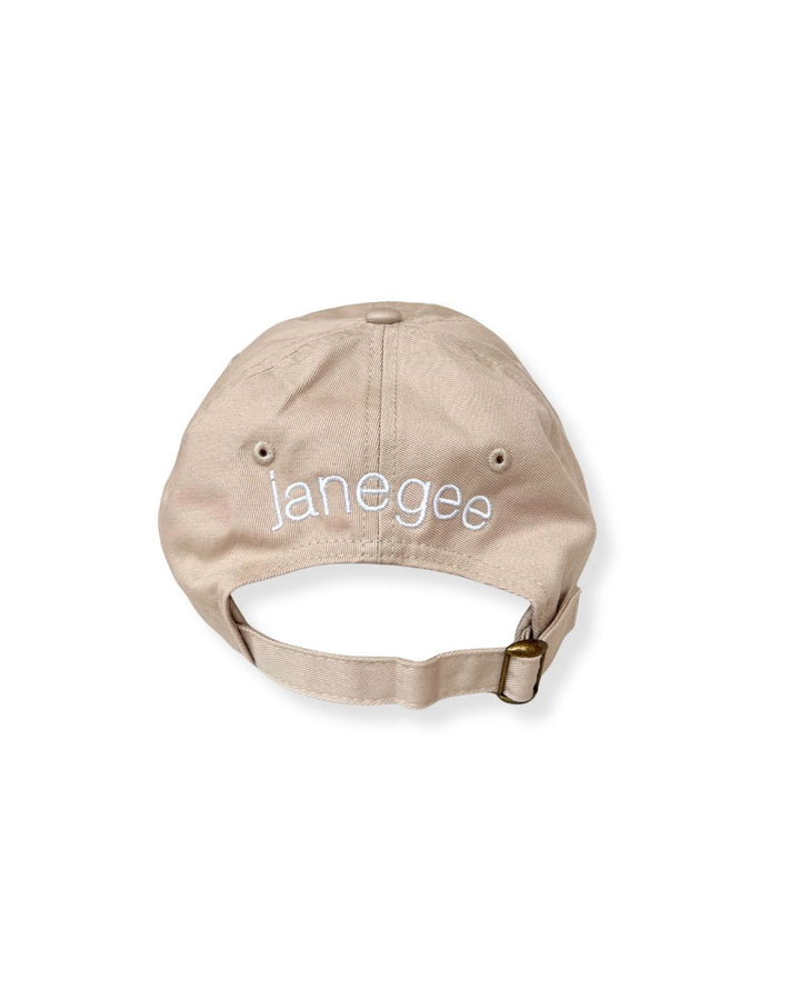 Back view of the beige janegee Everyday Botanical Cap with white embroidered janegee logo and adjustable brass buckle strap on a white background
