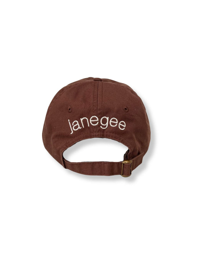 Back view of the brown janegee Everyday Botanical Cap with cream embroidered janegee logo and adjustable brass buckle strap on a white background.